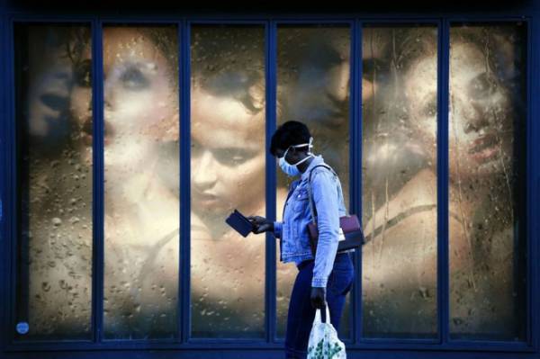 Một phụ nữ đeo khẩu trang bước qua cửa sổ của cửa hàng tại Paris hôm 14/4. .